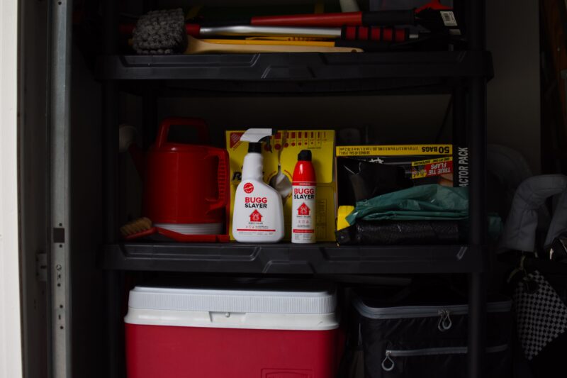 Spray bottle and can of insecticide sit on storage shelf in garage
